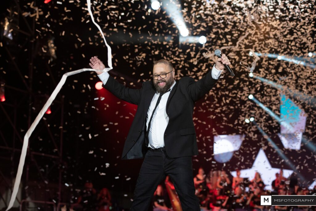 Man celebrating onstage in a suit with confetti