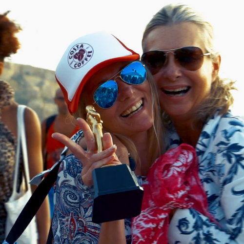 2 woman laughing holding a trophy and posing with a peace sign
